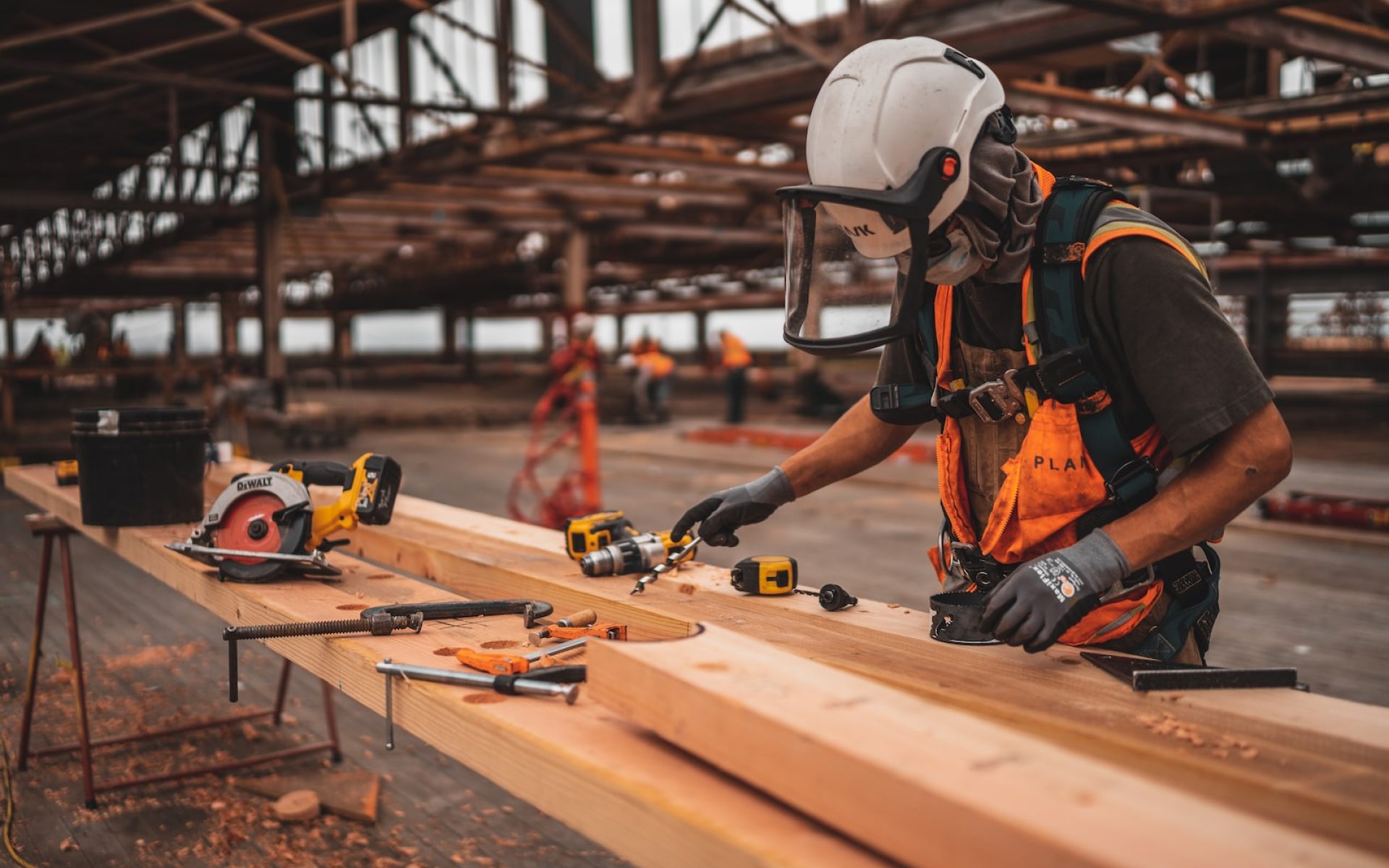 man in orange and black vest wearing white helmet holding yellow and black power tool