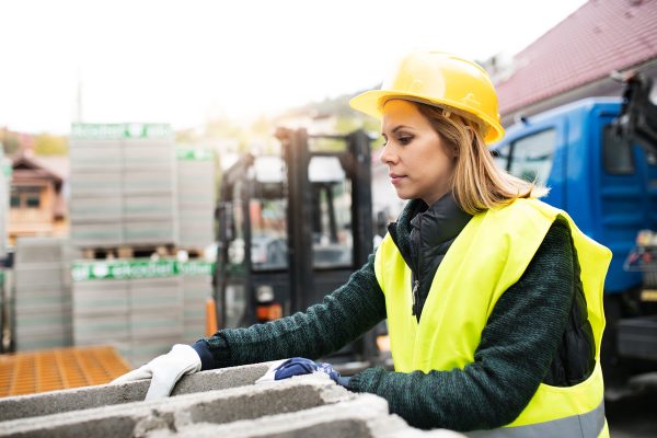 Female worker in an industrial area. Beautiful young woman working outside warehouse building.